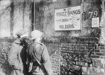 © IWM (Q 1633) Two British soldiers standing in front of a signboard in Fonquevillers advertising the 5th Division "Whizz Bangs" Concert Party, December 1916. The sign reads 'Whizz Bangs. Ensure bursts of laughter, fun, jollity, frivolity, merriment. No Duds.' Advert for the 5th Division 'Whizz Bangs Concert Party, December 1916
